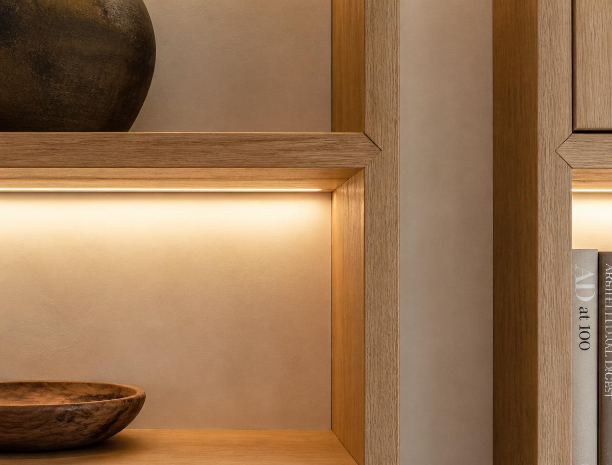 Detail of white oak built-in shelving with integrated linear lighting against a warm plaster wall